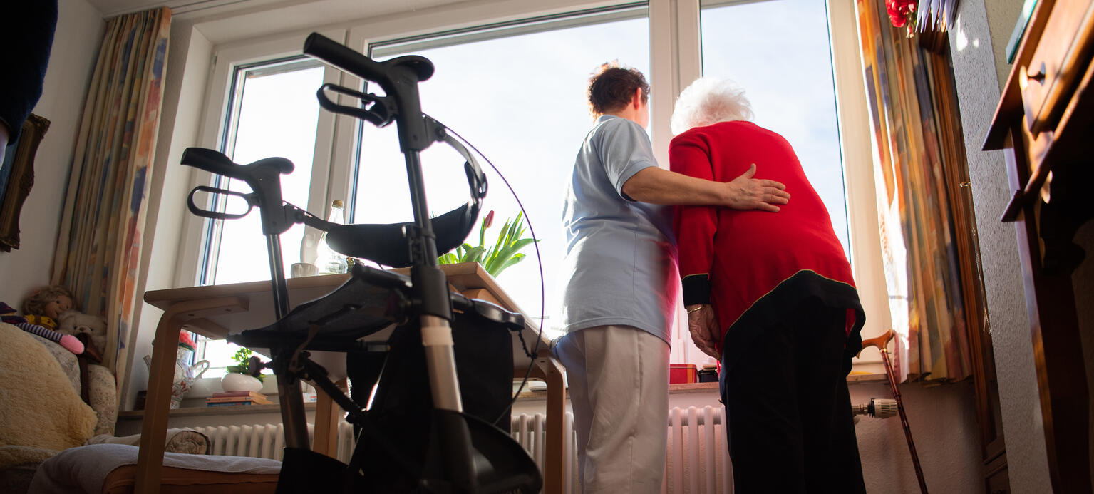 Eine Pflegerin (l) und eine Bewohnerin des Pflegeheims schauen zusammen aus einem Fenster 