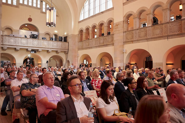 Hier wird das Auditorium gezeigt mit vielen Teilnehmern
