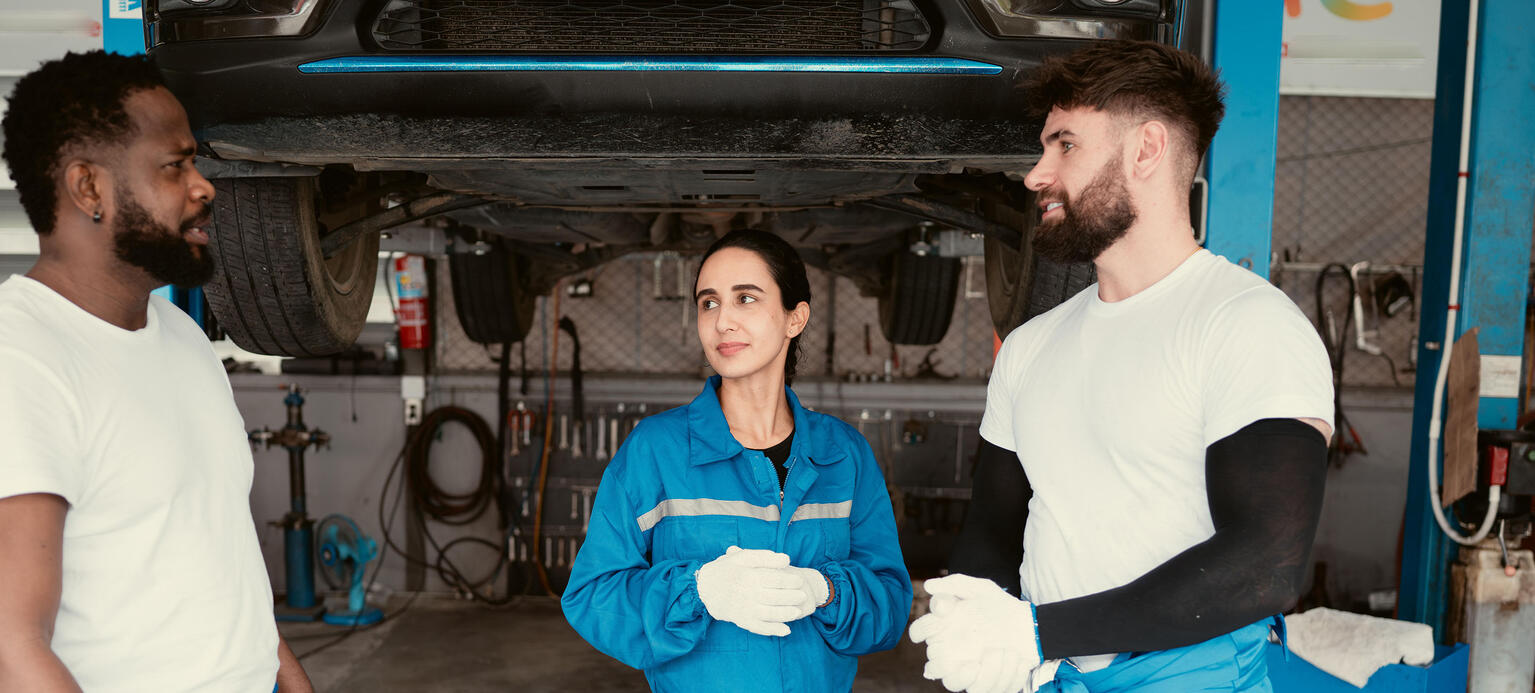 Portrait of smiling team of mechanics in auto repair shop, Talking one another while standing under car 