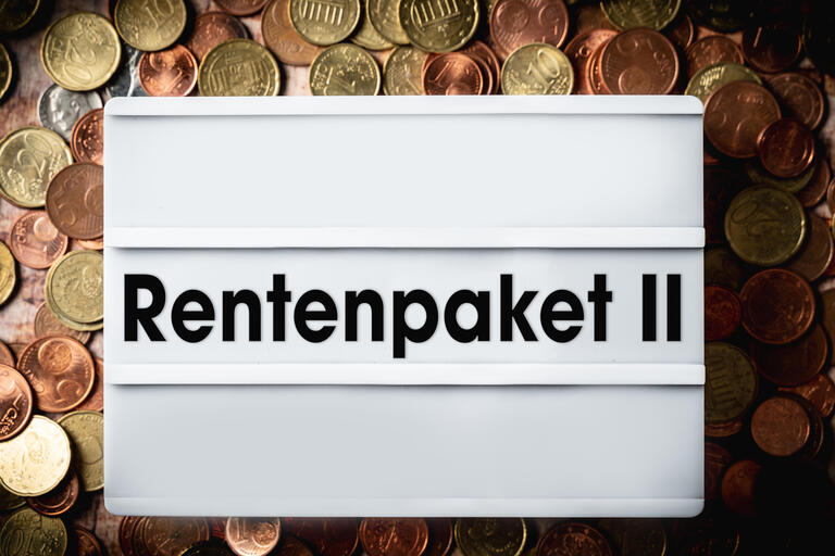 Aufschrift 'Rentenpaket 2' auf einer Tafel umgeben von Euro Münzen.