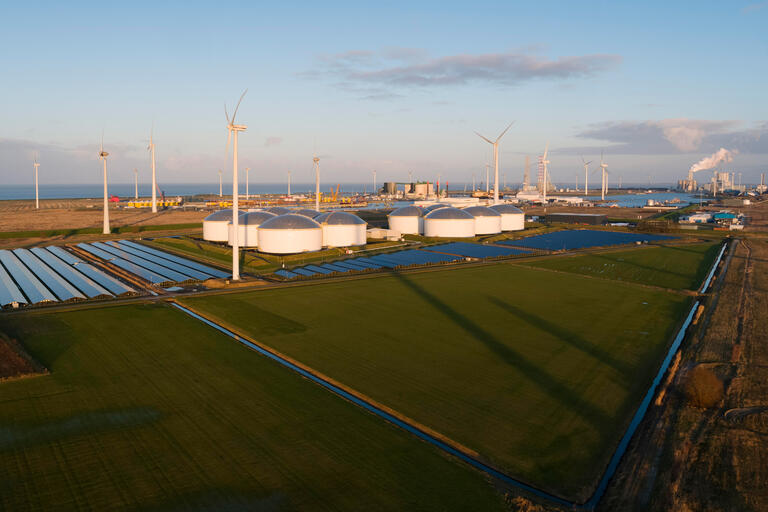 Wind turbines near solar panels with crude oil storage and coal fired power stations