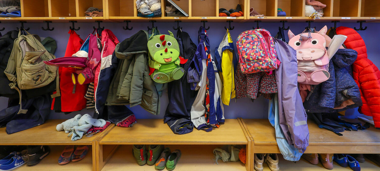 Maentel, Jacken, und Einhorn Rucksaecke von Kindern haengen an einer Garderobe in einem Kindergarten.