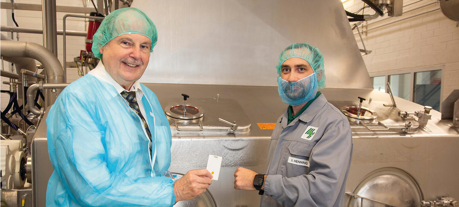 Bei der Firma Finzelberg in Andernach piept‘s, wenn sich Beschäftigte zu nah kommen. Betriebsratsvorsitzender Wolfgang Hell (l.) und Viktor Henning vor der Trocknungsanlage. Die Abstandskarte in Hells Hand gibt Signal, wenn 1,5 Meter Abstand unterschritten werden.
